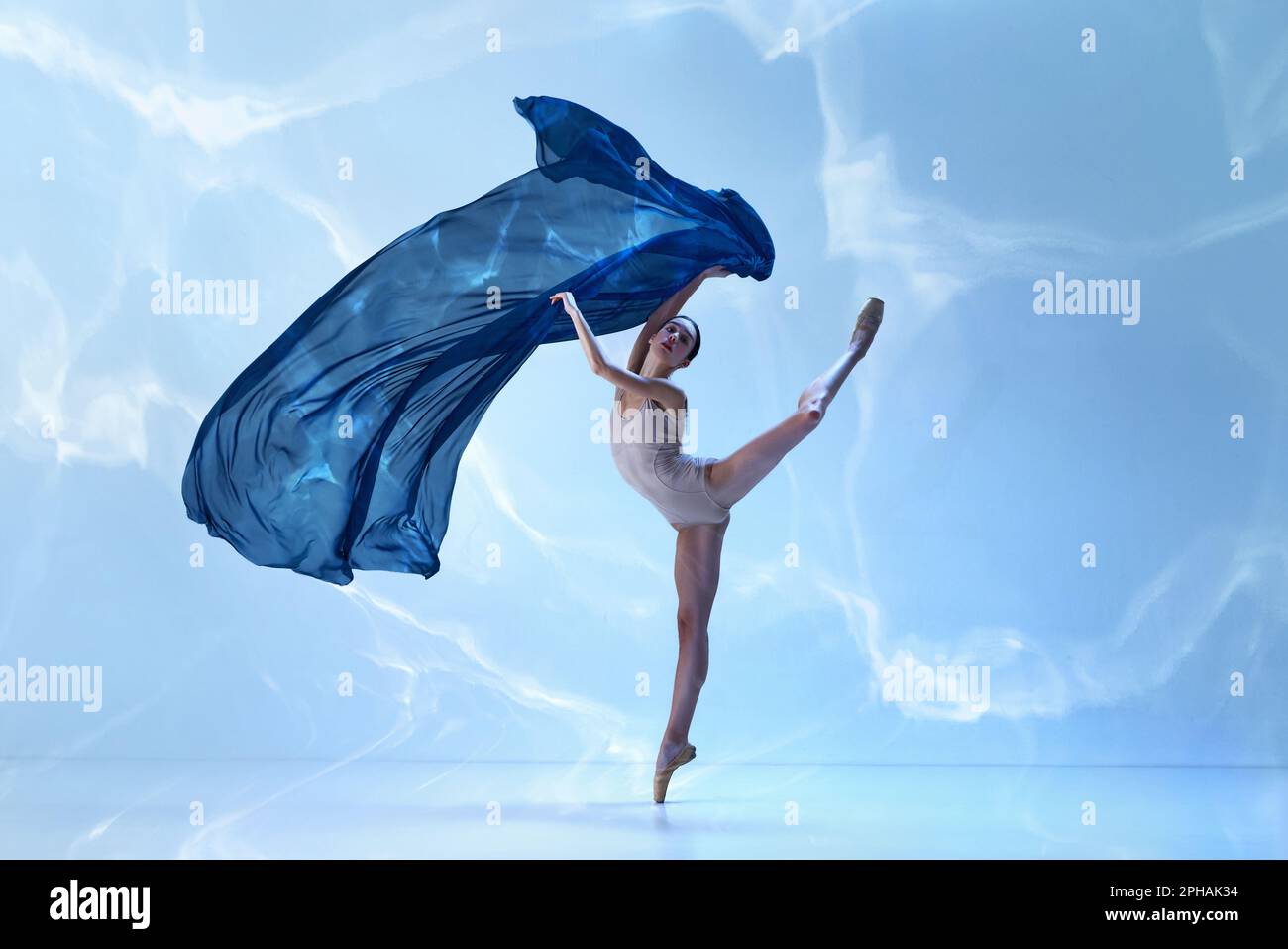 Young and graceful ballet dancer jumping with fabric over blue ...