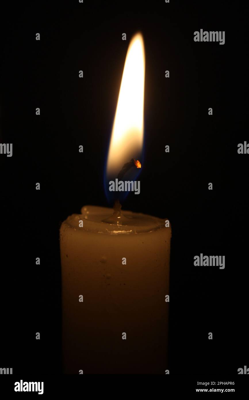 A single lit candle in a dark setting emits a plume of blue smoke ...