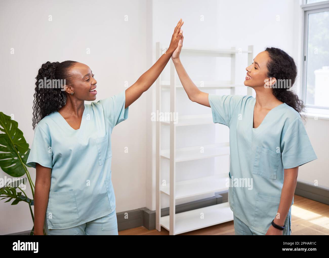 Two female doctors high five in clinic, wearing scrubs celebrate