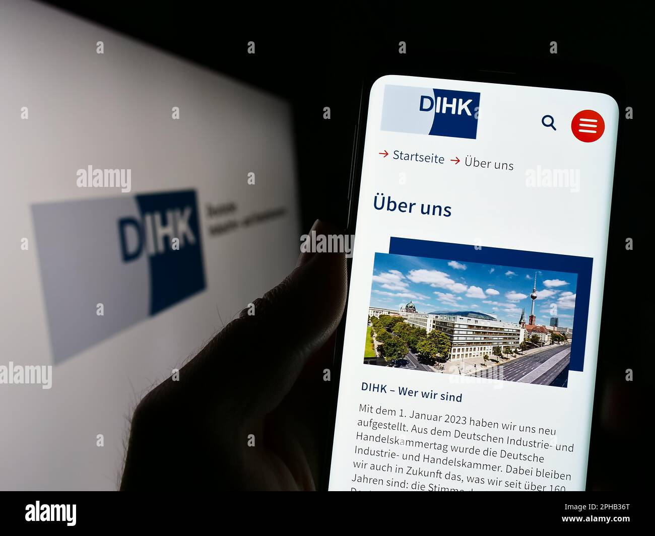 Person holding cellphone with website of Deutsche Industrie- und Handelskammer (DIHK) on screen with logo. Focus on center of phone display. Stock Photo