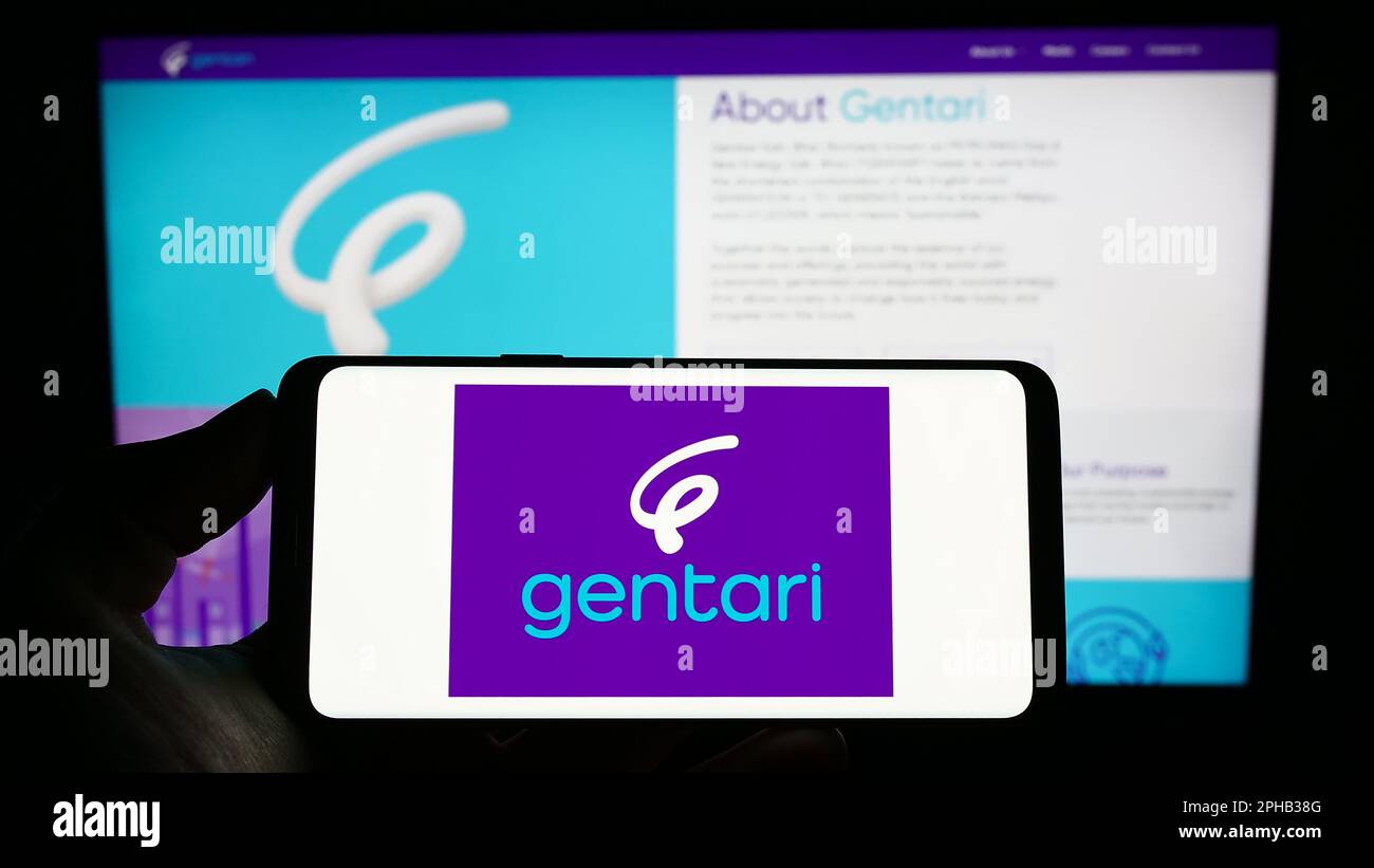 Person holding mobile phone with logo of Malaysian energy company Gentari Sdn. Bhd. on screen in front of web page. Focus on phone display. Stock Photo
