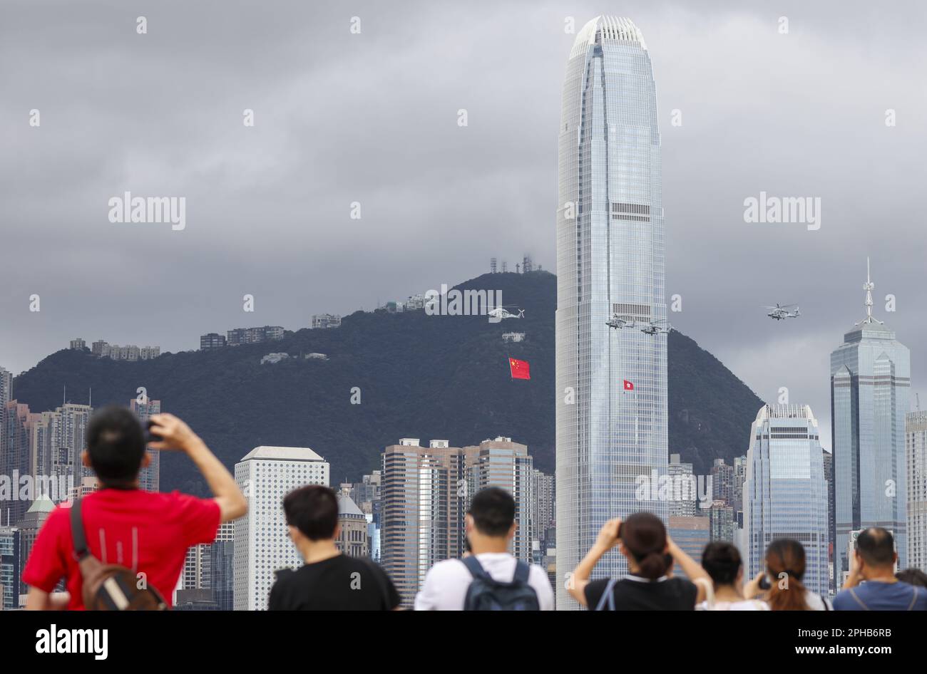 Members of the public watch the Government Flying Service's helicopters carrying the national and SAR flags fly past and sea parade during the flag-raising ceremony at Golden Bauhinia Square in Wan Chai to celebrate the 25th anniversary of the establishment of the HKSAR, viewing from the Tsim Sha Tsui promenade, while police patrol and stand guard. 01JUL22 SCMP / Nora Tam Stock Photo