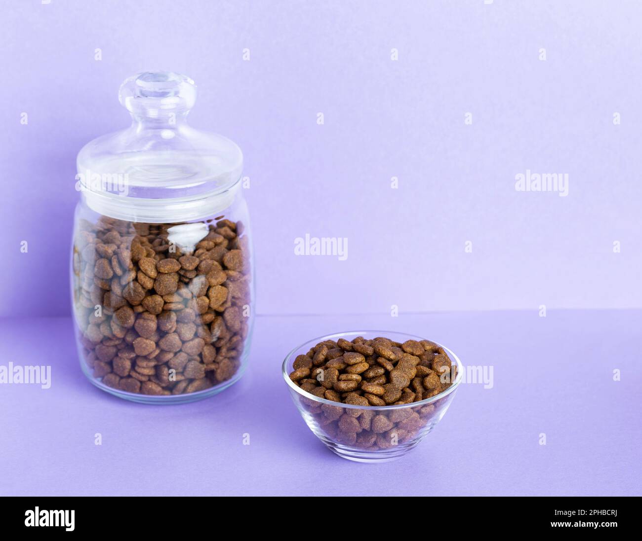 Dry pet food in a glass jar and bowl closeup on a lilac background