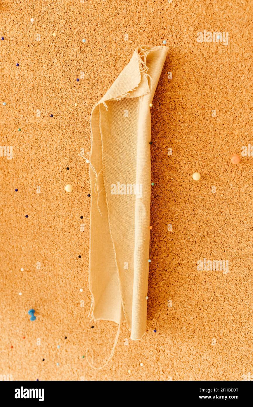 A vertical close-up image of a single piece of white fabric pinned to a corkboard Stock Photo