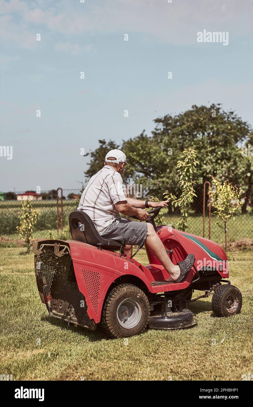 Man mowing his lawn using riding lawnmower. Man maintaining grass in his garden beside house Stock Photo