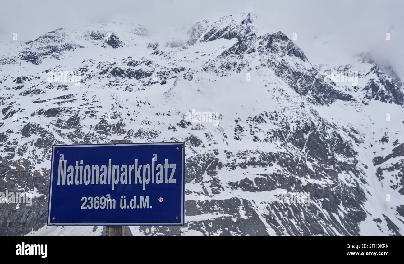 Snow-capped Alpine peaks behind a sign for a high-altitude national park site in Austria. Stock Photo