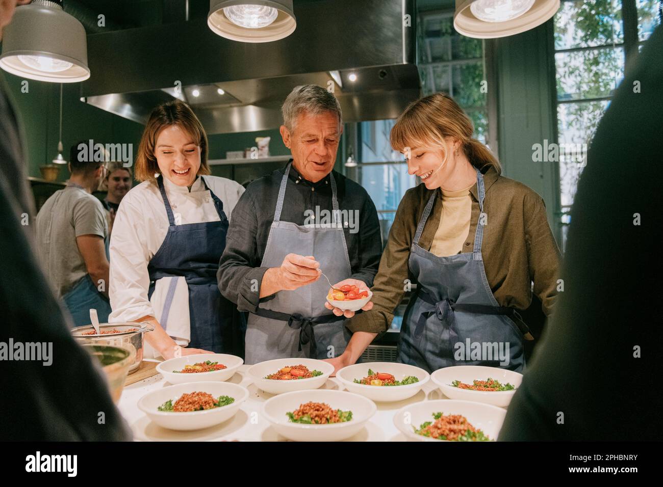 Smiling female chef with students plating during cooking class in kitchen Stock Photo