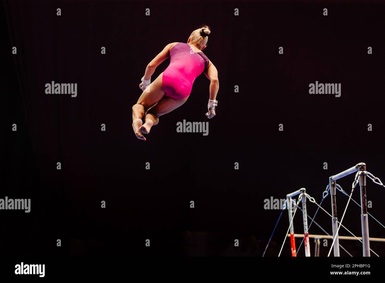 female gymnast performing somersault gymnastics on uneven bars, black