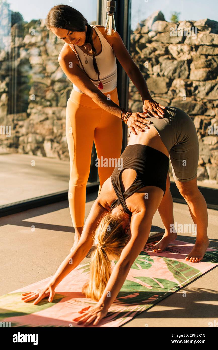 Female instructor supporting woman doing yoga at retreat center Stock Photo