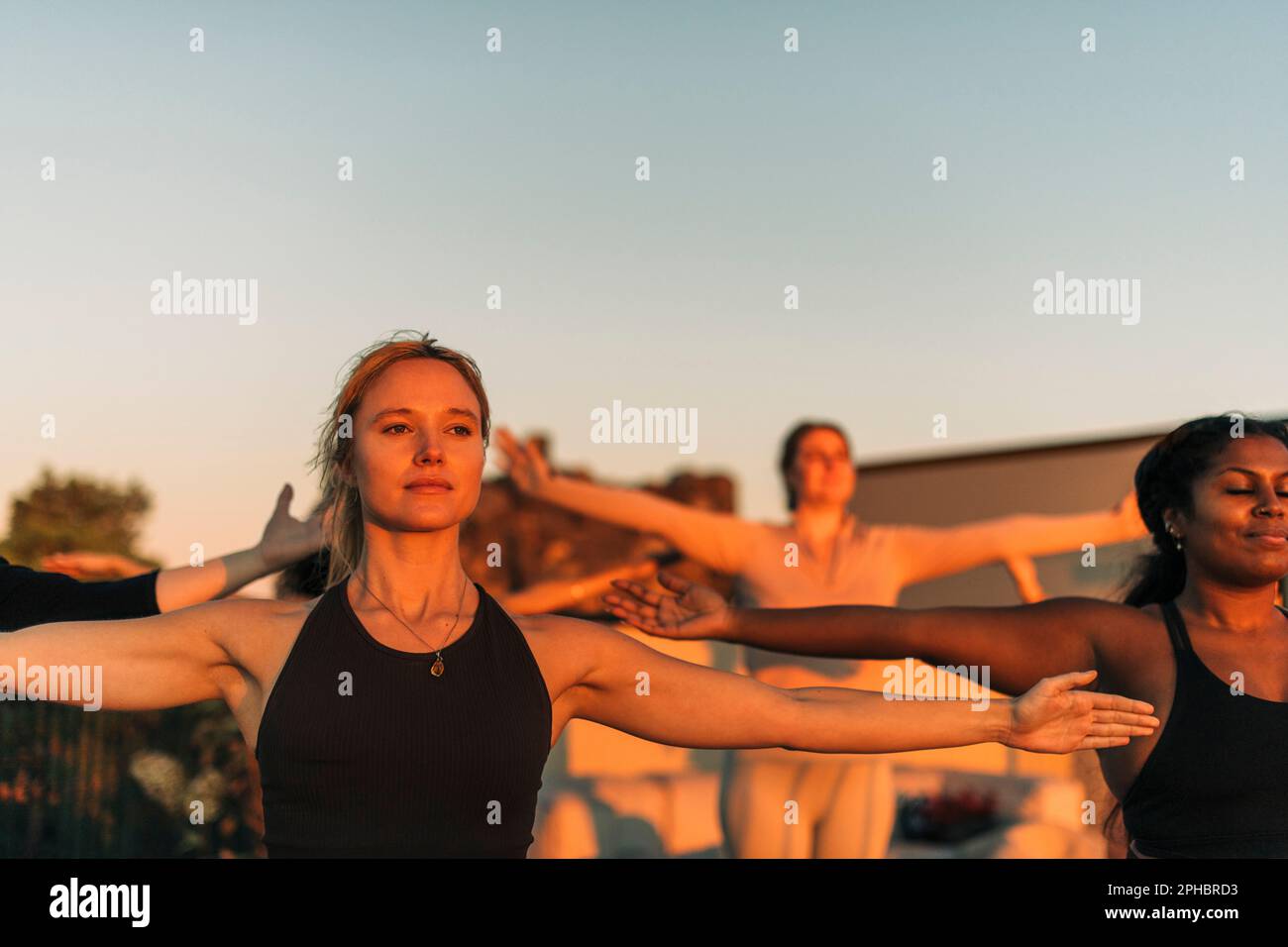 Woman with arms outstretched exercising with female friend at sunset Stock Photo