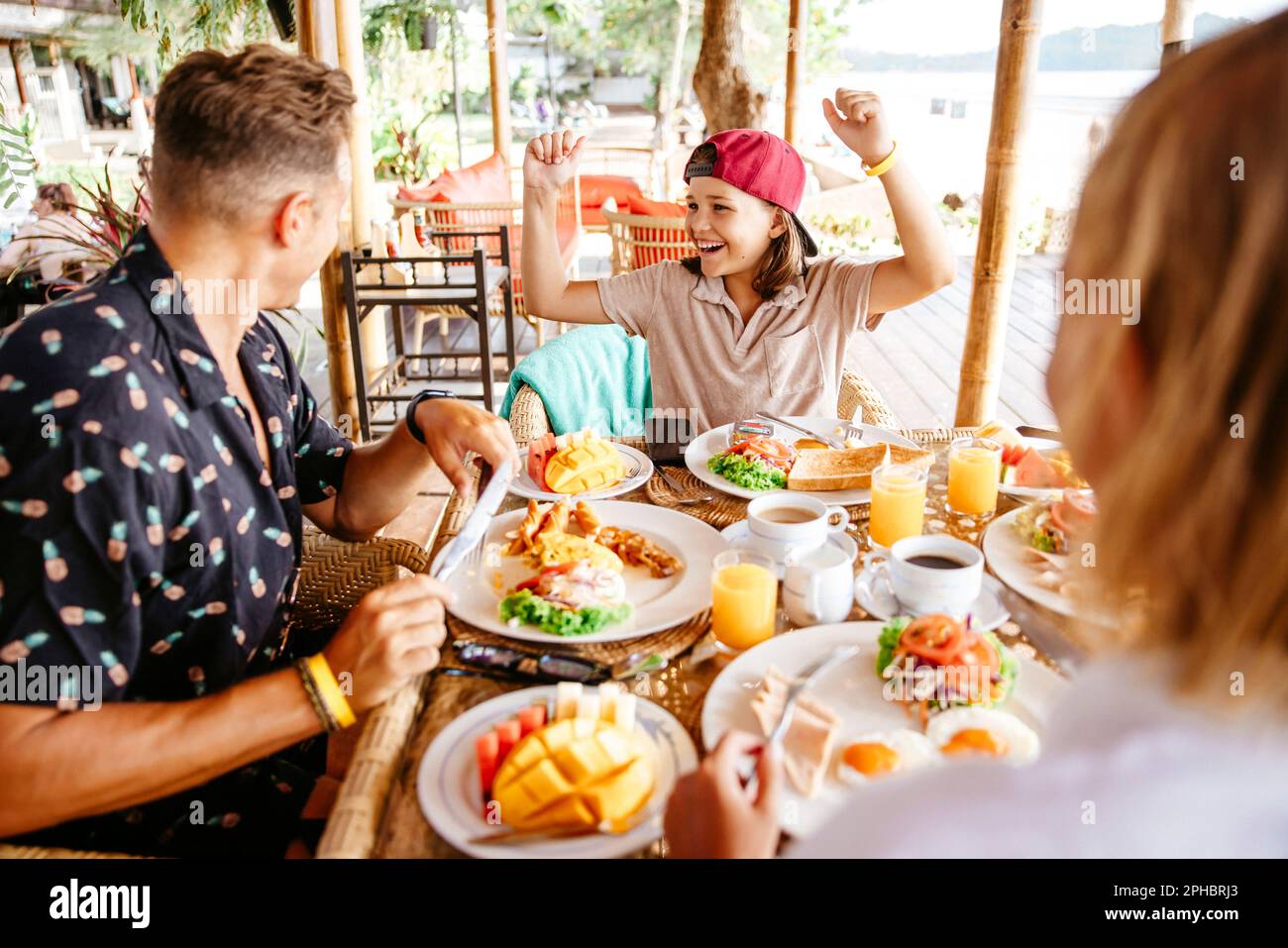 Happy girl clenching fists while parents having breakfast at table in resort Stock Photo