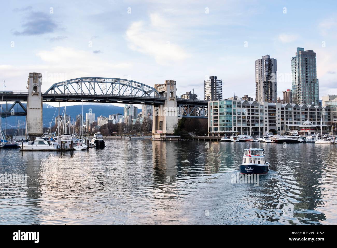 An aquabus water taxi departs from Granville Island, with the Burrard Street bridge and skyline of Vancouver at sunset in the distance. Stock Photo