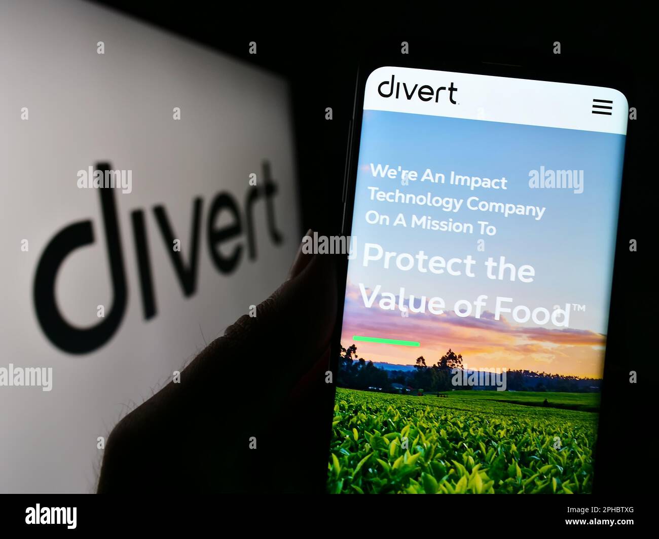 Person holding cellphone with website of US food technology company Divert Inc. on screen in front of logo. Focus on center of phone display. Stock Photo