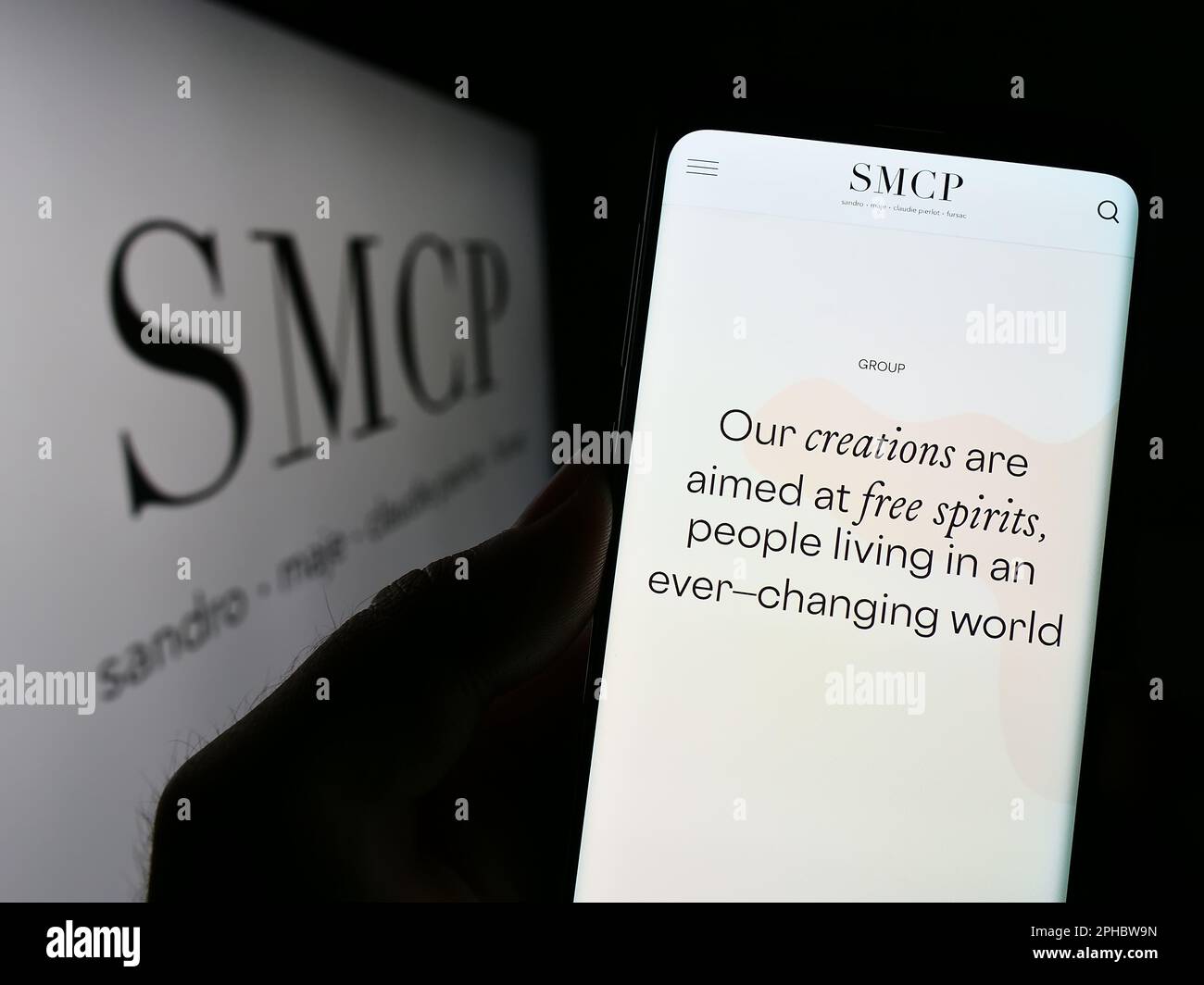 Person holding smartphone with web page of French luxury fashion company SMCP S.A. on screen in front of logo. Focus on center of phone display. Stock Photo