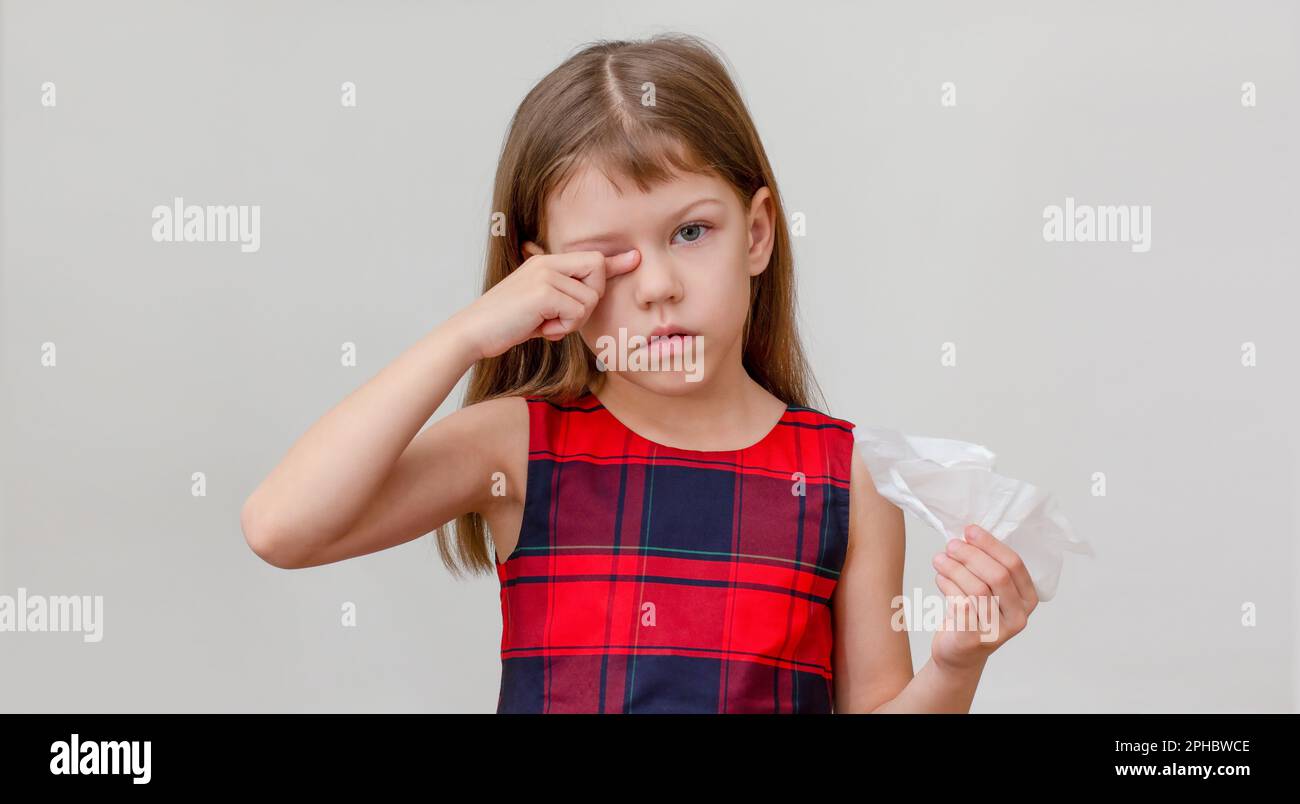 Child scratching eye and holding napkin in hand showing allergy