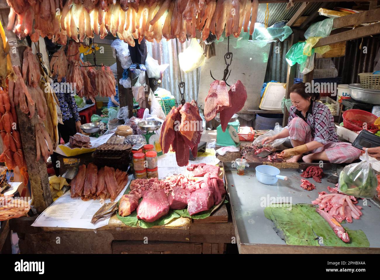 Woman cutting and selling meat at a local market in Phnom Penh, Cambodia. Butcher shop. Raw meat hanging in the shop. Stock Photo