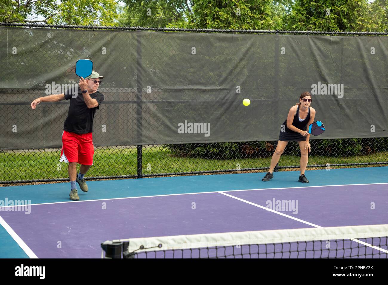 A pickleball player serves while his partner prepares for a return on a