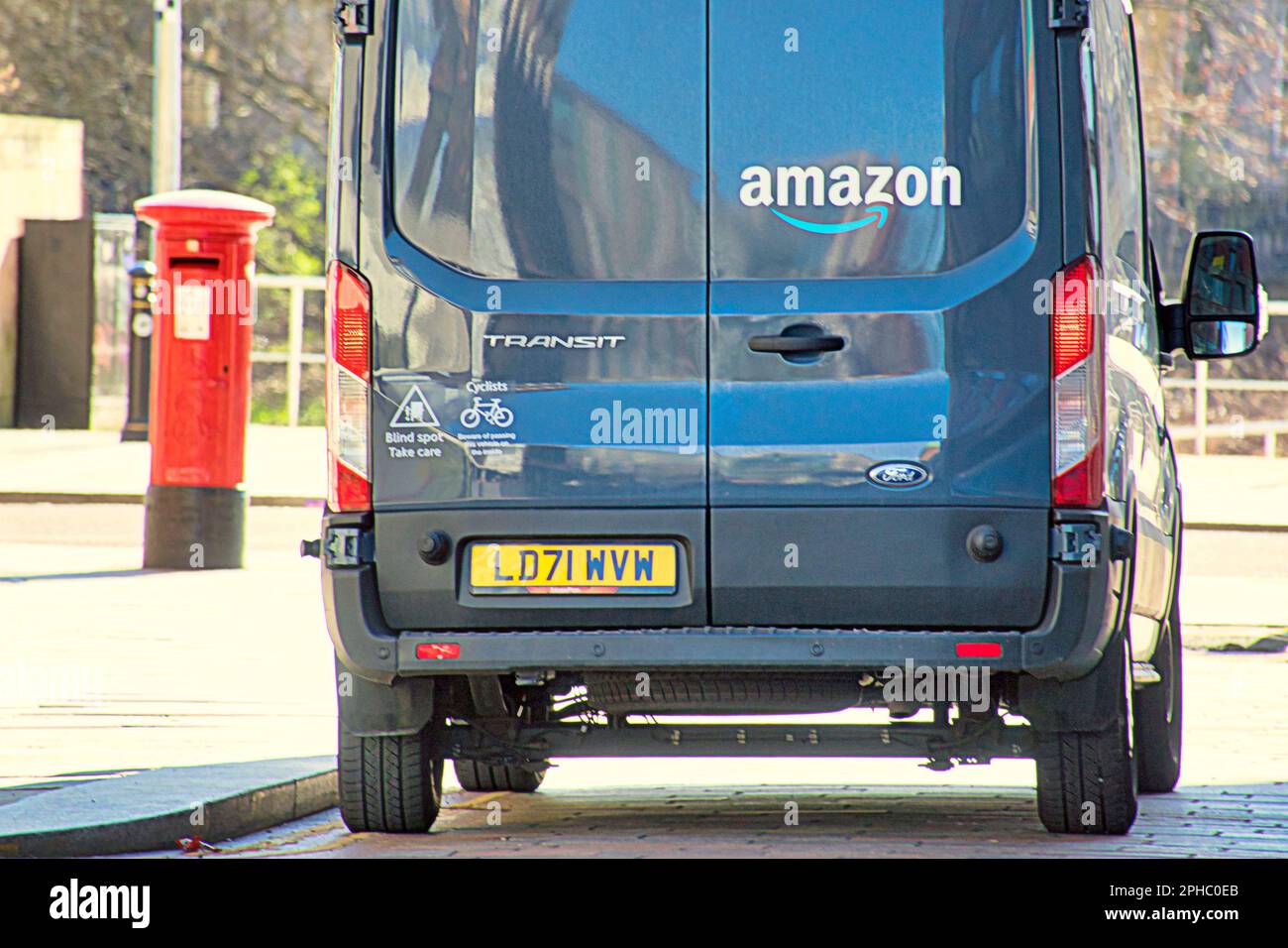 amazon delivery van in front of red royal mail post box to illustrate amazon using royal mail to deliver packages Stock Photo