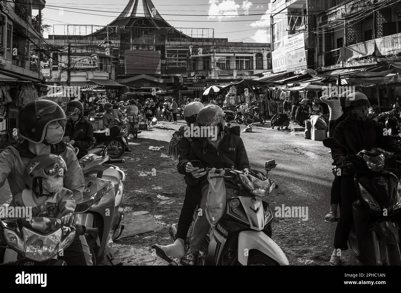 A young couple on a Yamaha scooter stop to look at a mobile phone outside the busy central market in Pleiku, in the central highlands in Vietnam. Stock Photo