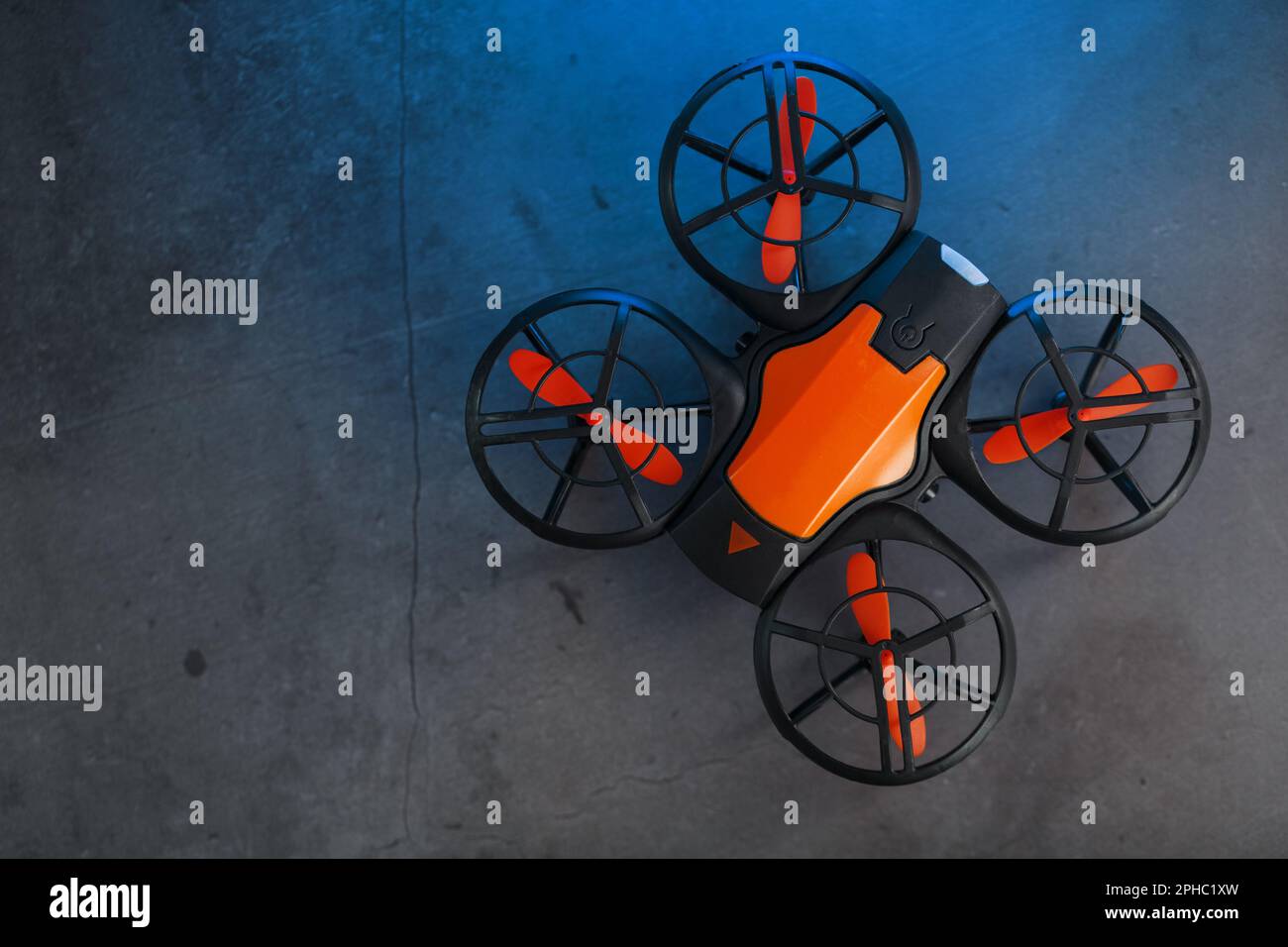 A reconnaissance quadcopter drone with an orange body and blue LED backlight on a dark background Stock Photo