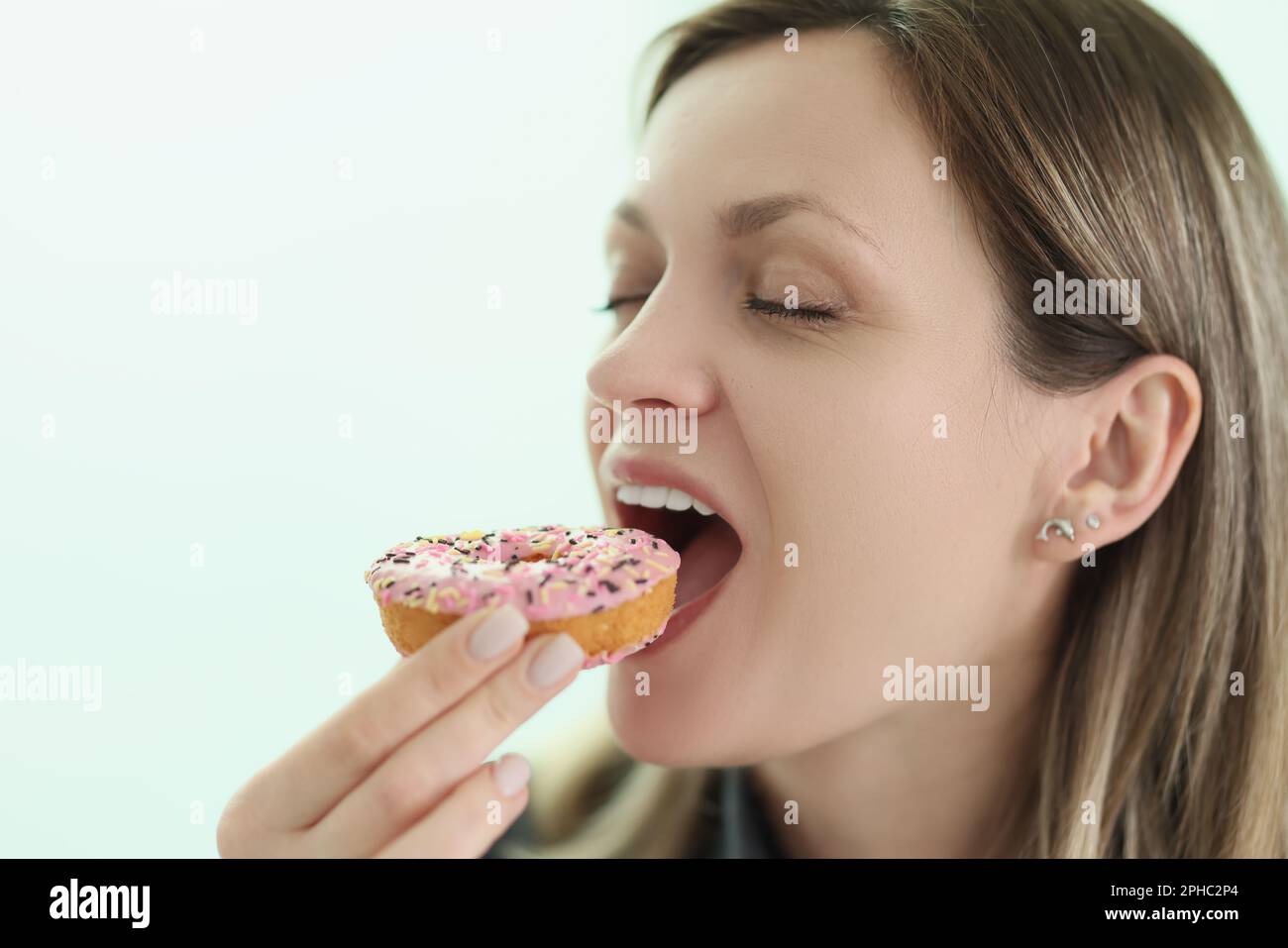 Happy woman bites delicious donut on light background Stock Photo