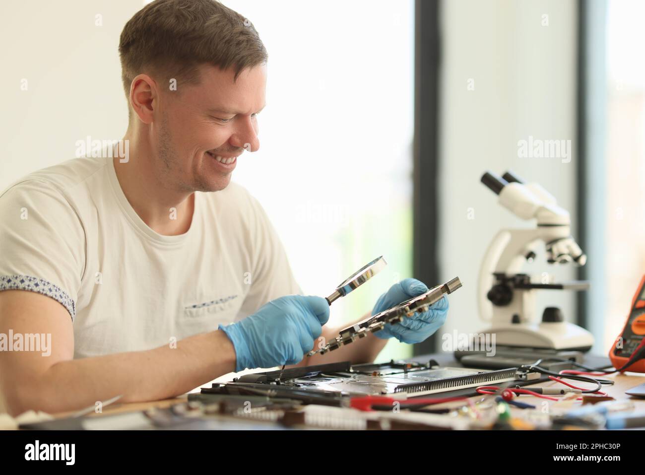 Smiling man studies broken motherboard in repair workshop Stock Photo
