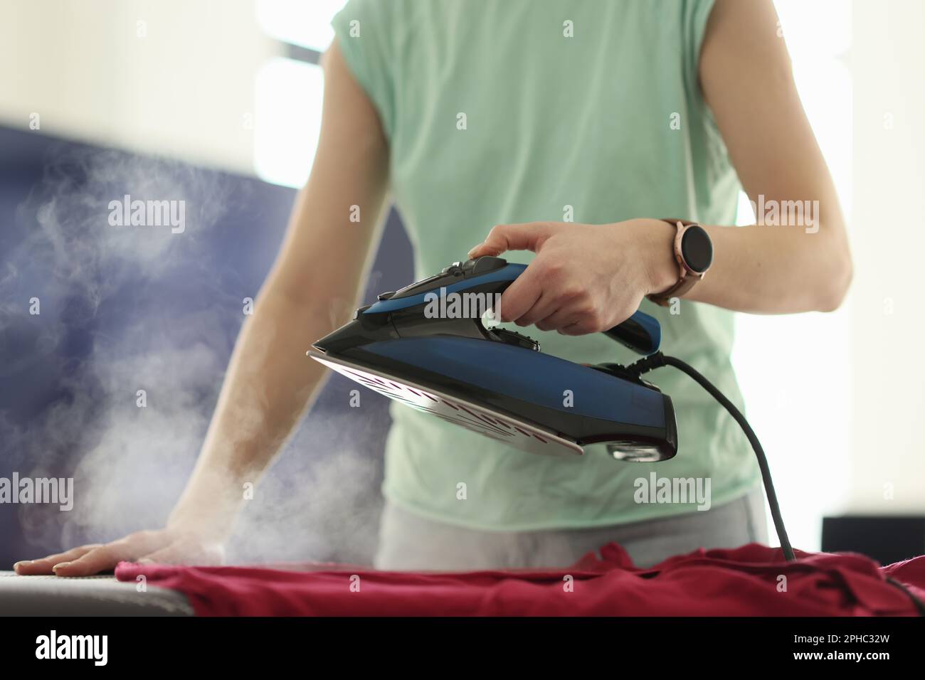 Woman irons clothes with hot steam appliance at home Stock Photo