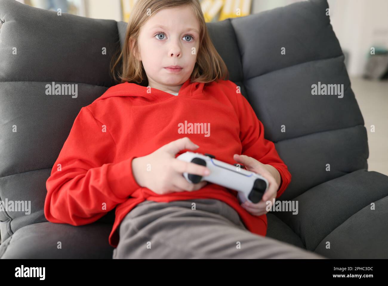 Focused teenage girl in red hoodie holds gaming console Stock Photo
