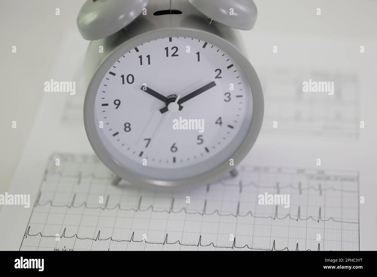 Alarm clock stands on cardiogram papers on table in hospital Stock Photo