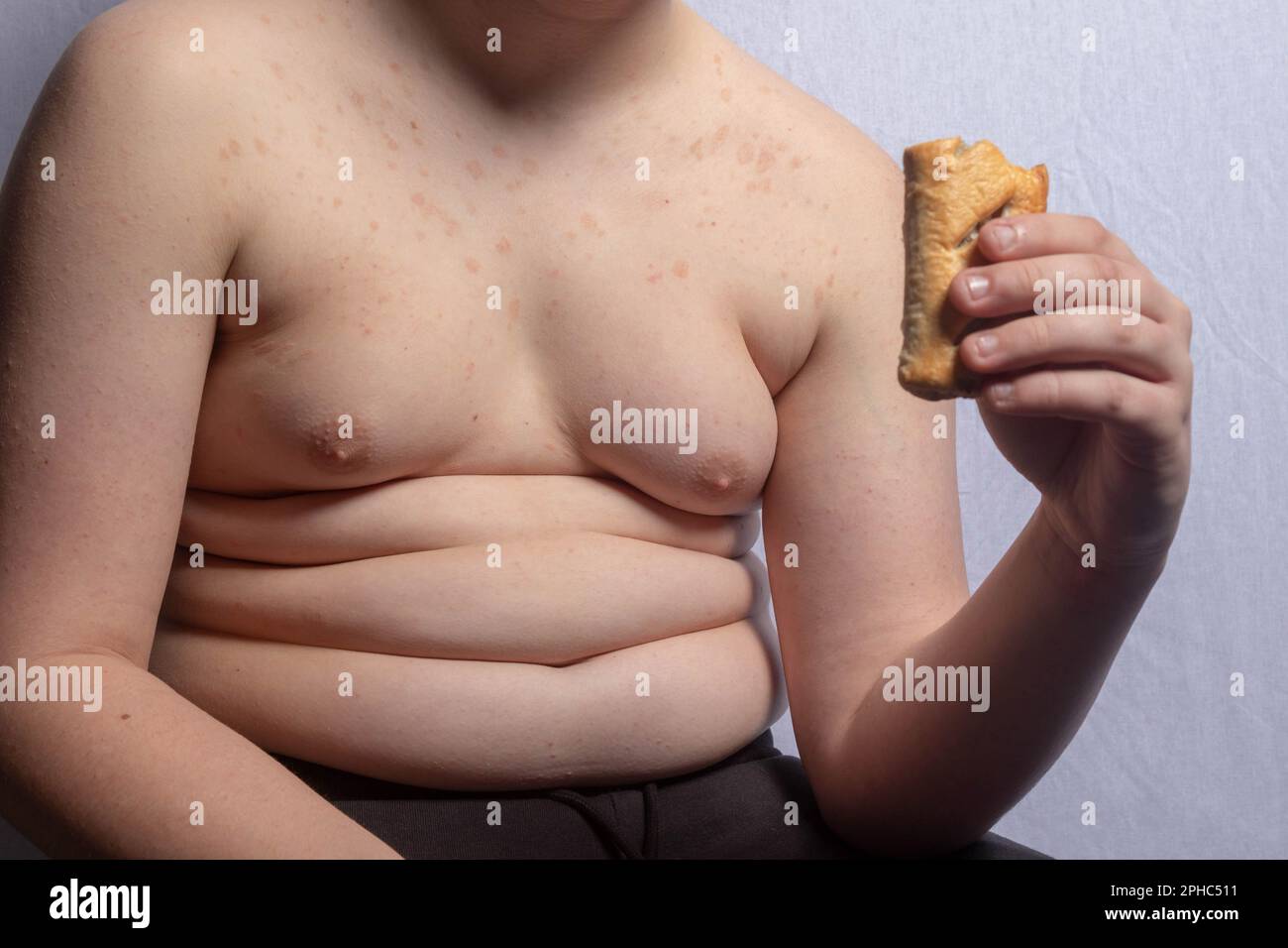 An overweight caucasian teenage boy eating a sausage roll Stock Photo