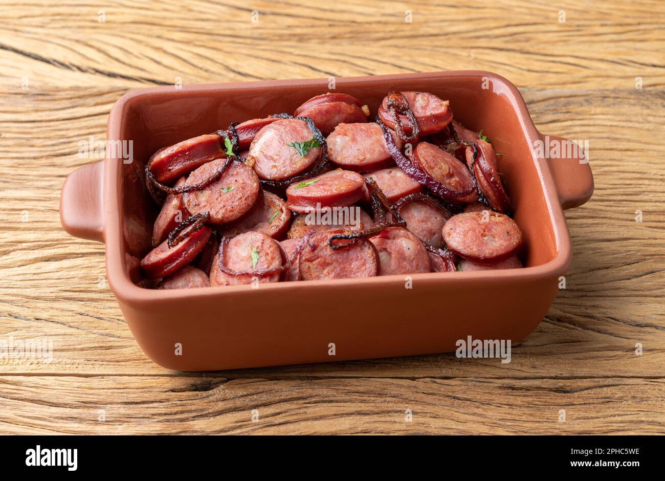 Grilled calabrese sausage portion with onion over wooden table. Stock Photo