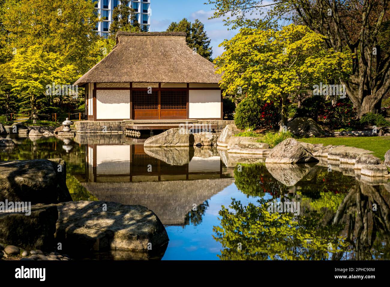 The picturesque Japanese tea house in the morning sun, surrounding scenic rocks and nature mirroring in the water of a pond, a tranquil setting. Stock Photo