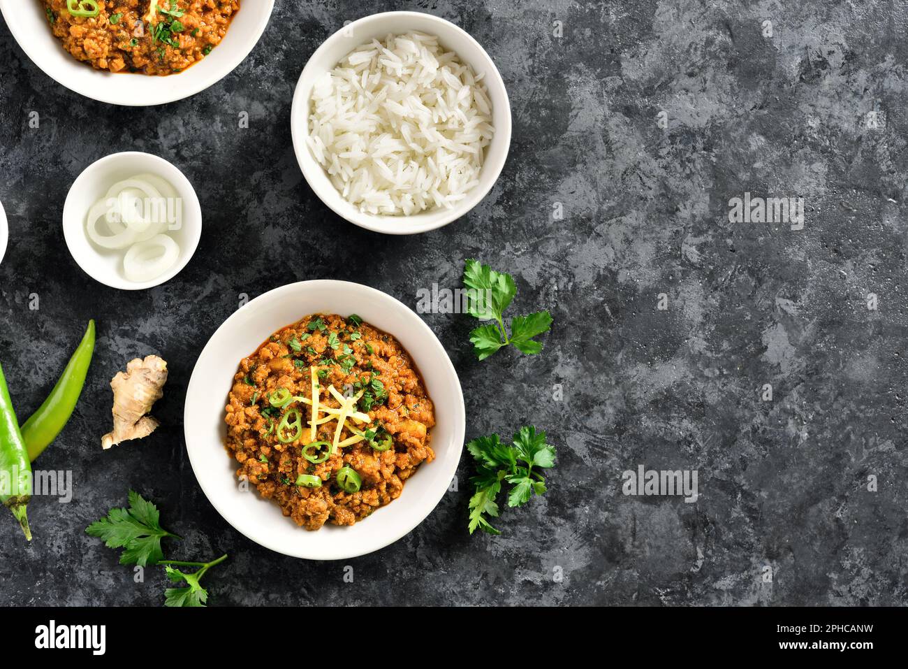 Bowls of keema curry and rice over dark stone background with free