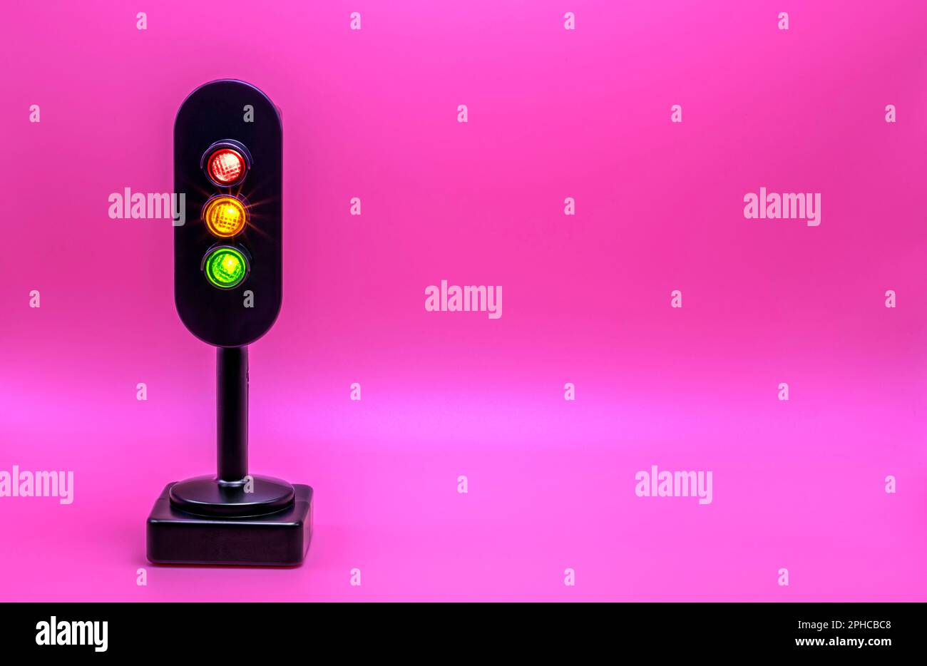 Miniature traffic light with red, orange and green light on. Studio shot. Pink empty background. Stock Photo