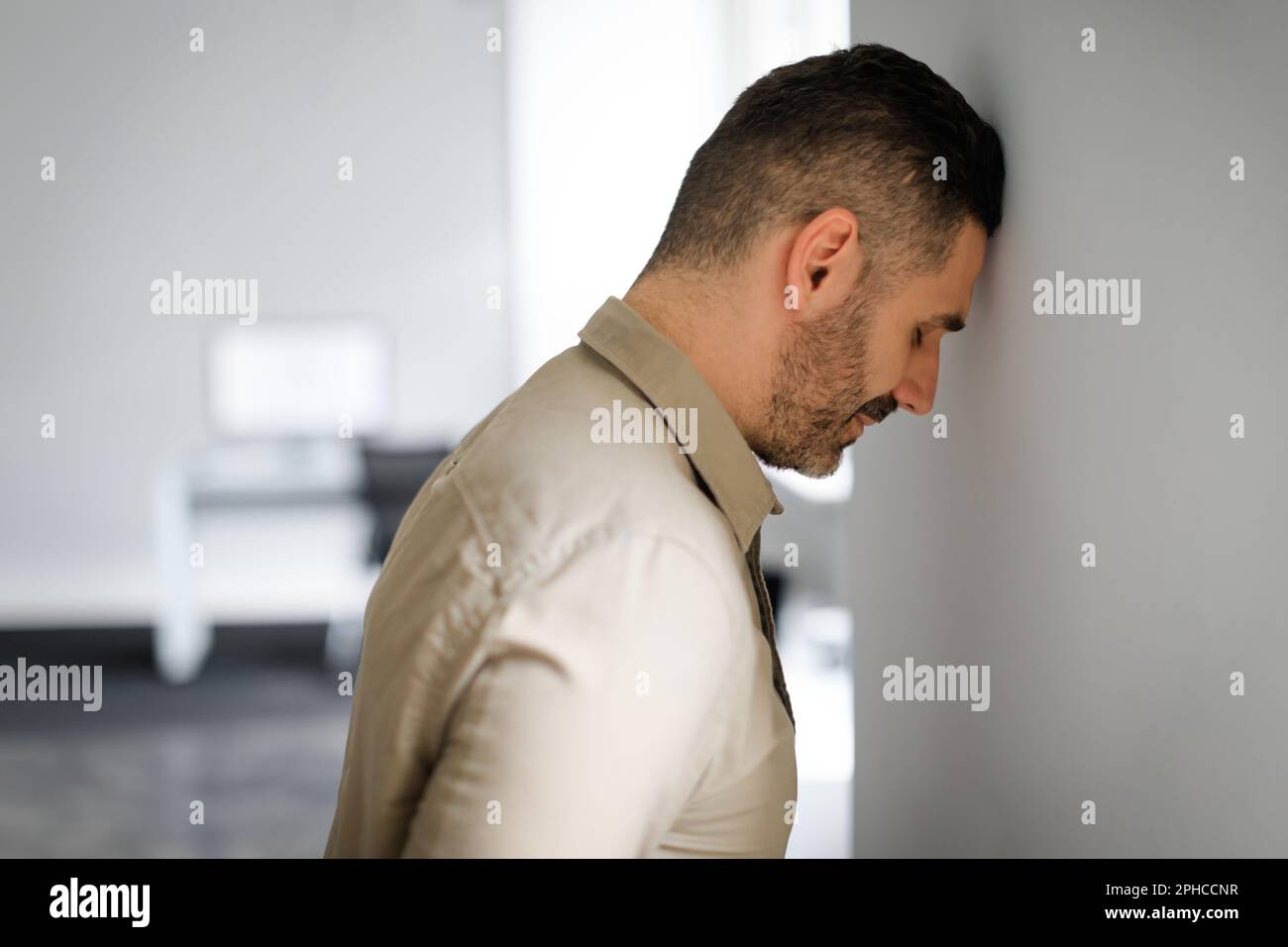 Upset middle aged businessman banging his head against wall in despair looking stressed, having problems at work Stock Photo
