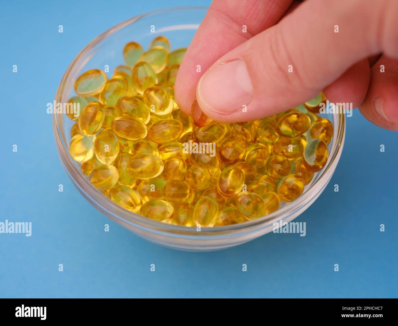 A woman taking a vitamin D3 softgel from a glass bowl of other softgels. Close up. Stock Photo