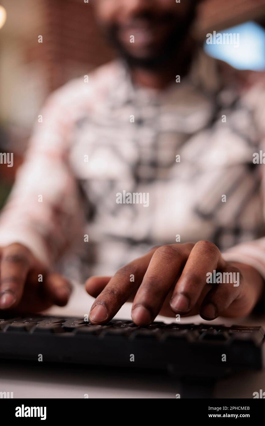 Closeup of african american coder writing software using computer keyboard while working remote from home living room. Selective focus on man freelancer hands typing text while programming. Stock Photo