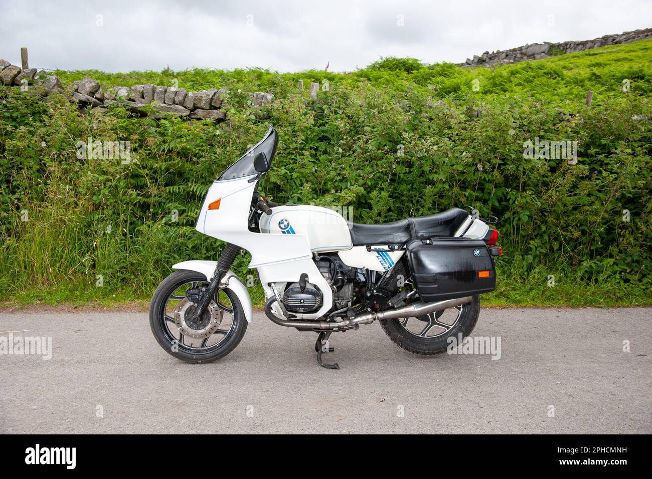 BMW R100 RS motocycle parked on a narrow country lane next to ferns and a dry stone wall in the Derbyshore Peak District, with Stanage Edge behind. Stock Photo