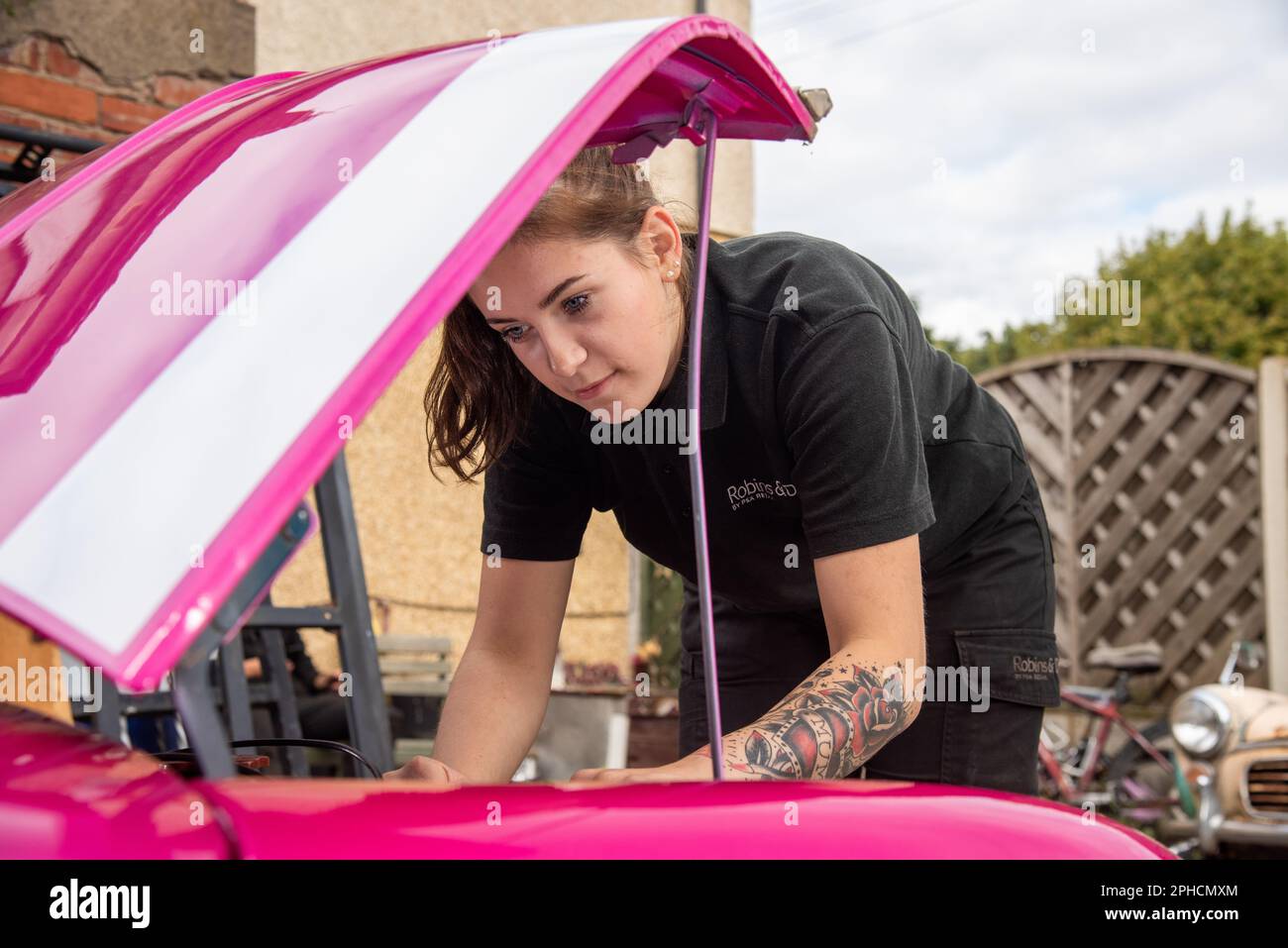 Young woman mechanic carrying out maintenance on a bright pink classic Austin Mini Stock Photo