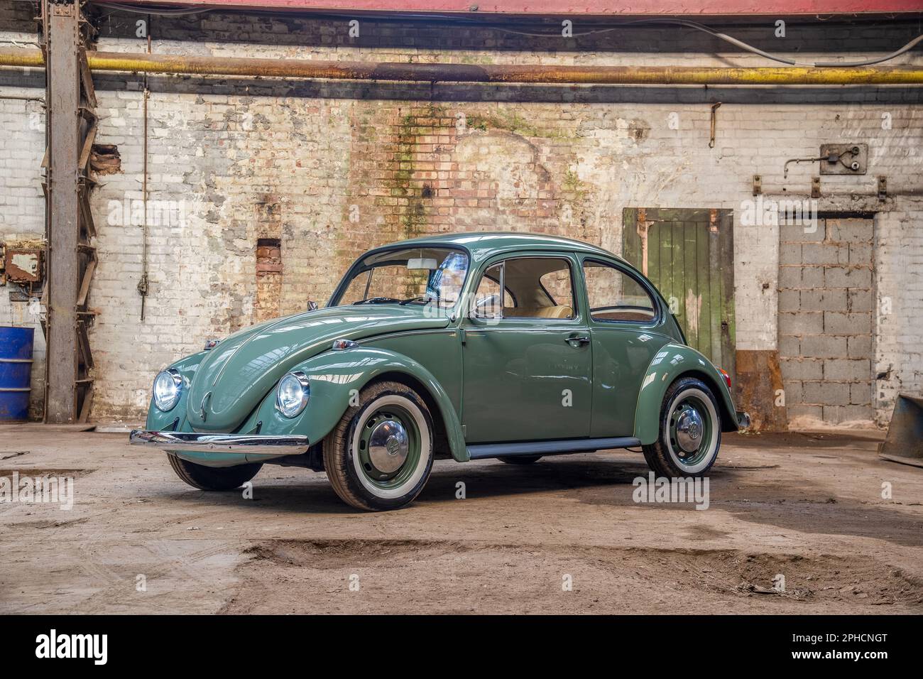 Green Volvkswagen Beetle with white walled tyres parked in an old engineering works Stock Photo
