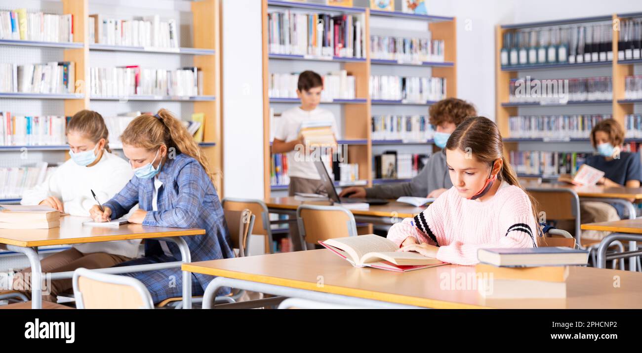 Portrait of preteen girl reading books in college library Stock Photo ...
