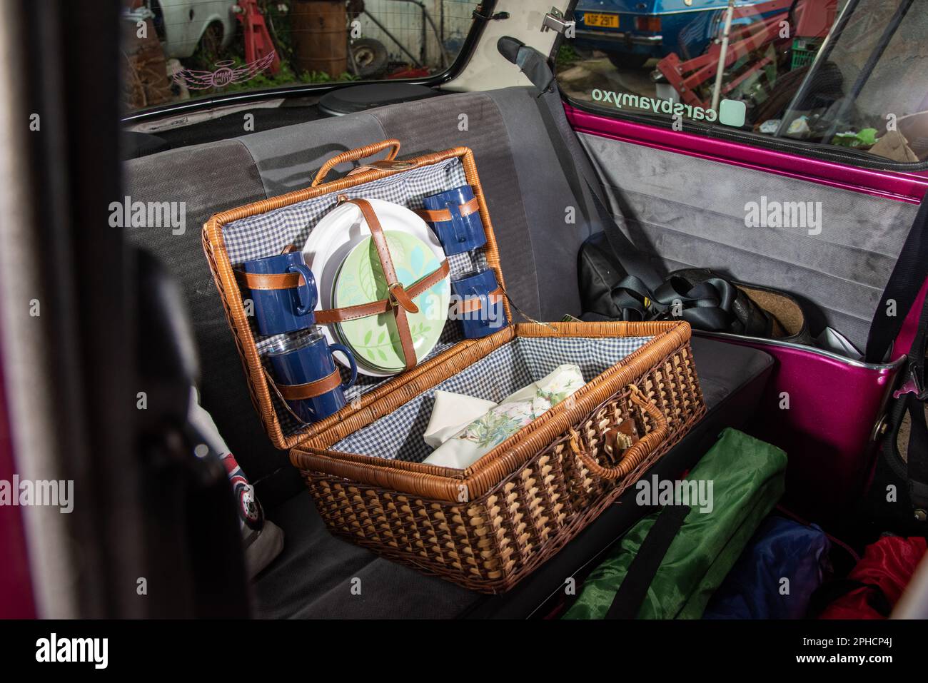 Open wicker basket picnic hamper and camping kit on the back seat of an