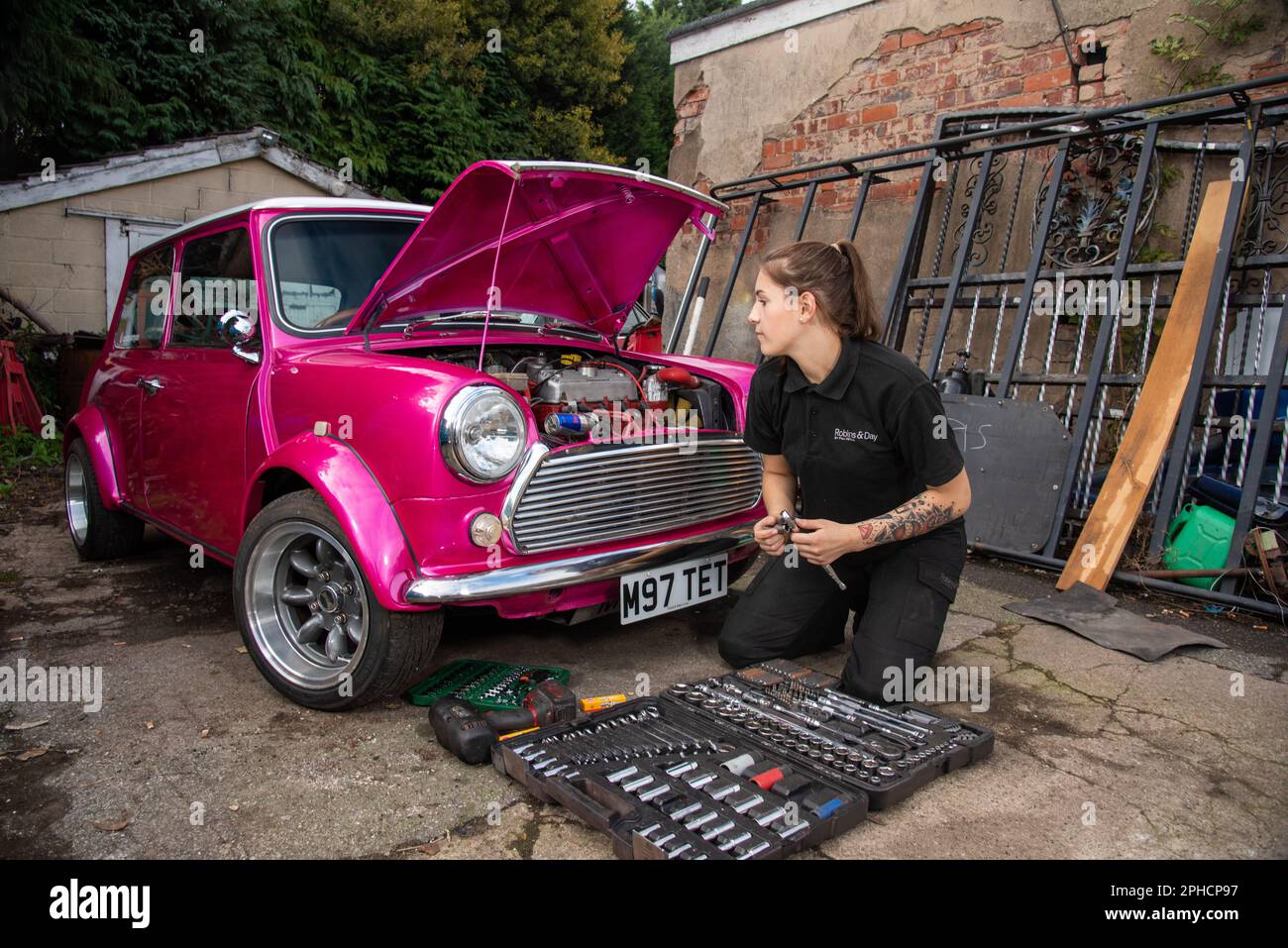 Young woman mechanic carrying out maintenance on a bright pink classic Austin Mini Stock Photo