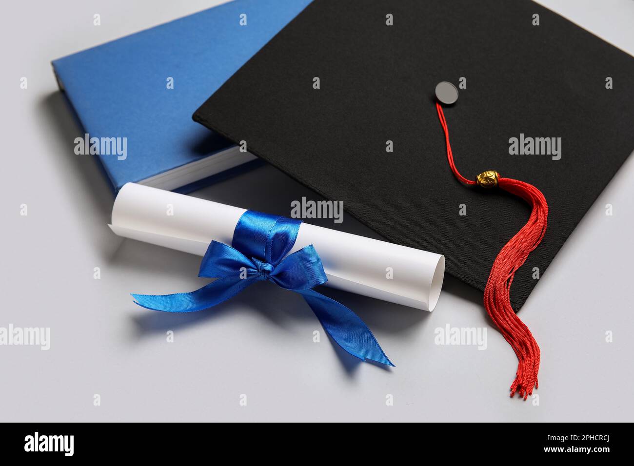 Diploma with blue ribbon, graduation hat and book on white background