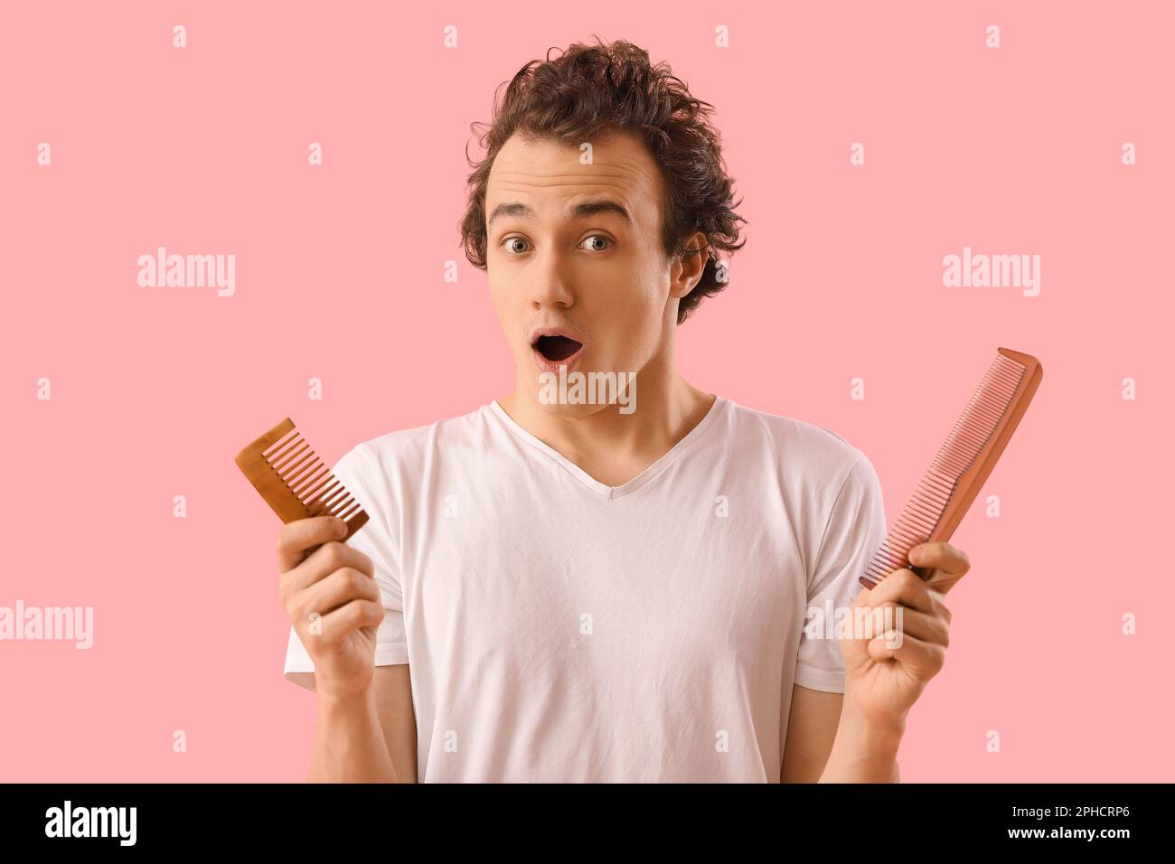 Shocked young man with hair loss problem and combs on pink background