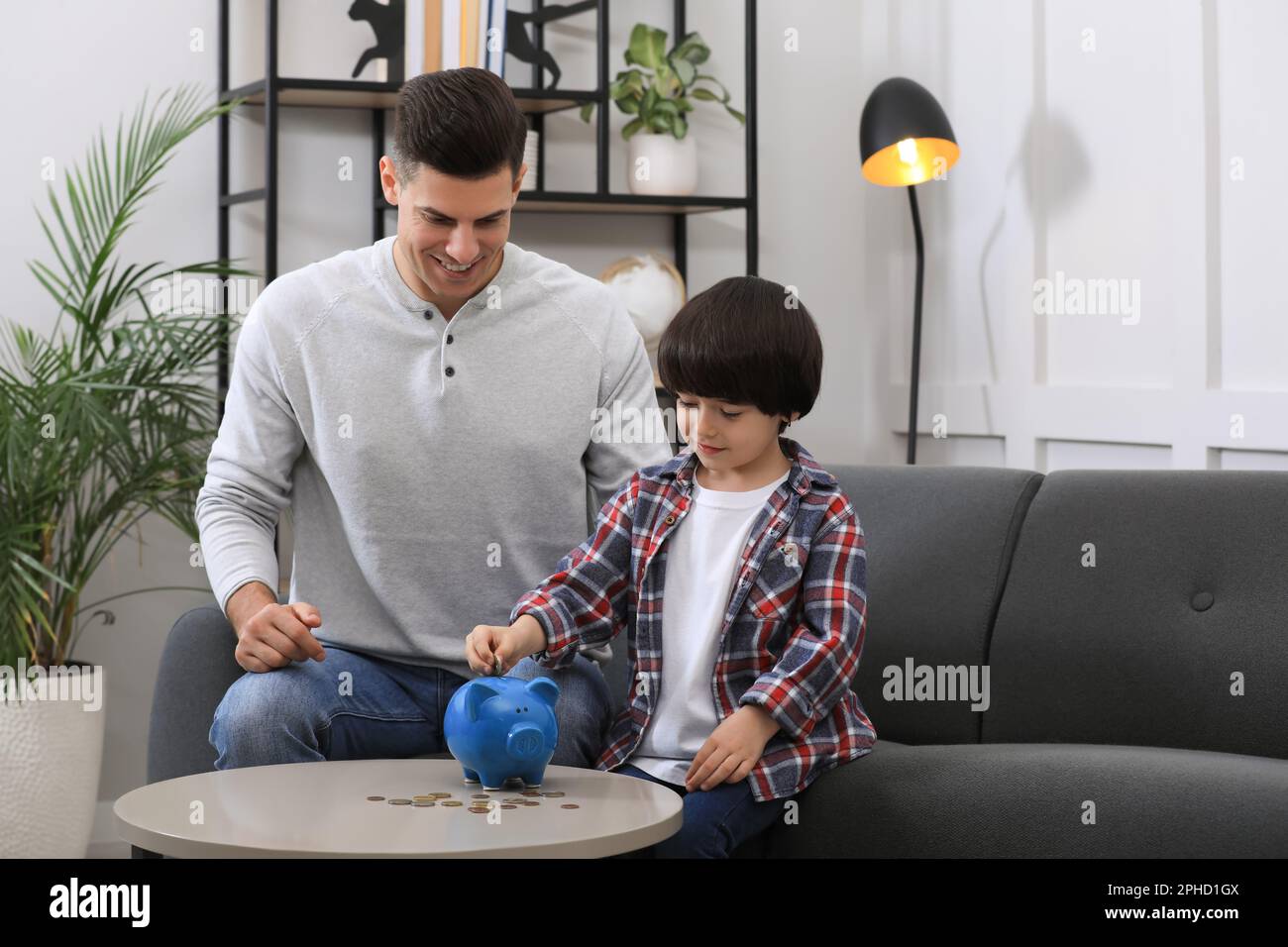 Little boy with his father putting coin into piggy bank at home Stock ...