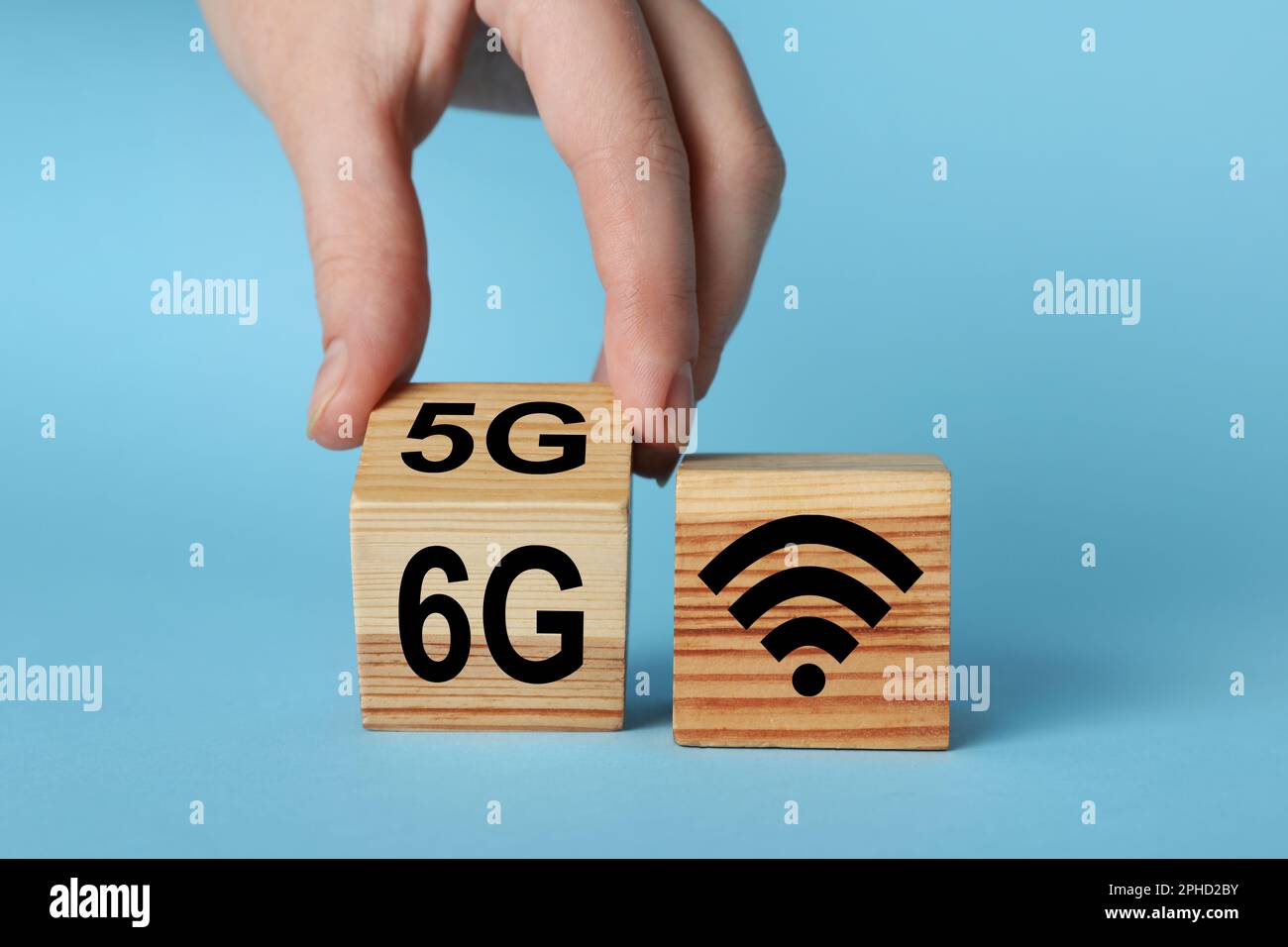 Man turning cube with 6G and 5G symbols near WiFi sign on light blue background, closeup Stock Photo