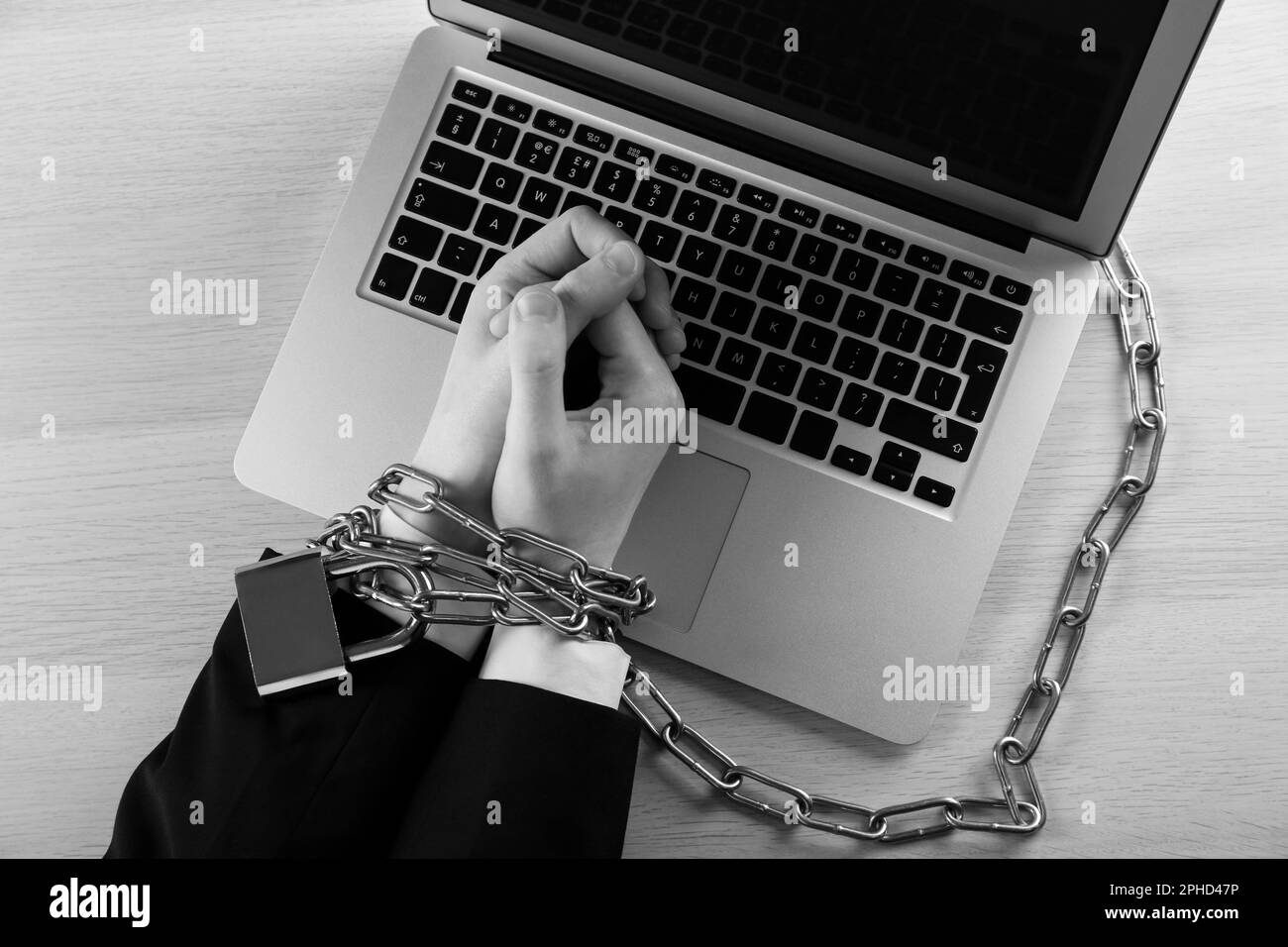 Top view of woman with chained hands and laptop at wooden table, black and white effect. Internet addiction Stock Photo