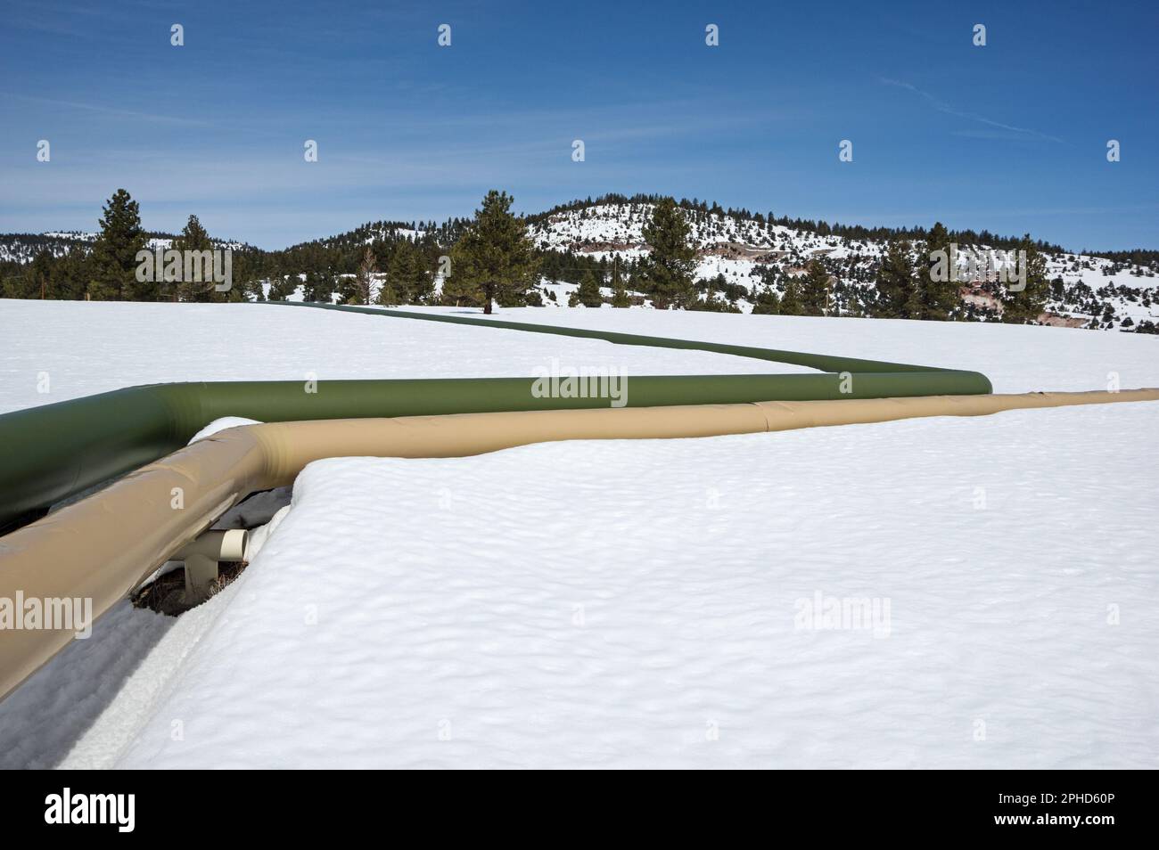 geothermal pipes in the snow with mountain behind Stock Photo