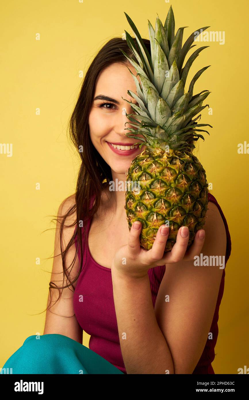 Woman holding a pineapple in front of her face wearing a red shirt in